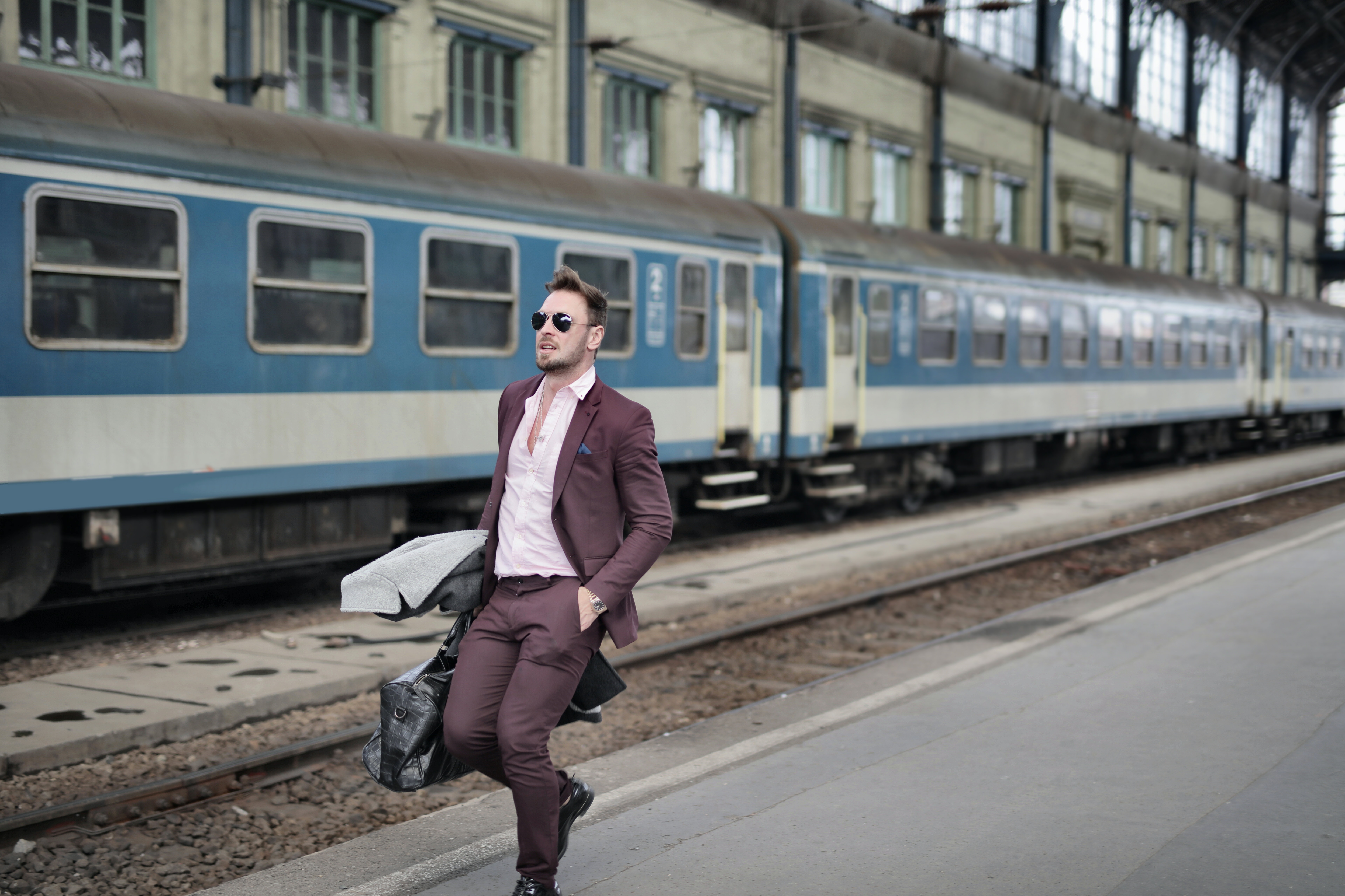 Man in Pink Dress Shirt and Brown Suit Carrying Luggage Walking Beside Train